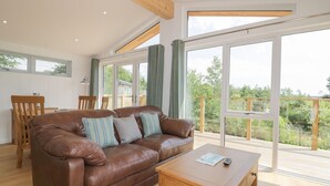 A spacious living room with a brown leather sofa, wooden coffee table, and large windows offering a view of the outdoors.