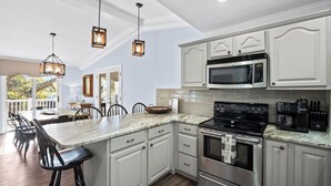 A modern kitchen with white cabinetry, a large island with bar stools, stainless steel appliances, and pendant lighting. - FrippLife, Walk to Beach, Golf Cart Included - 707 Bluefish (Fripp Island)