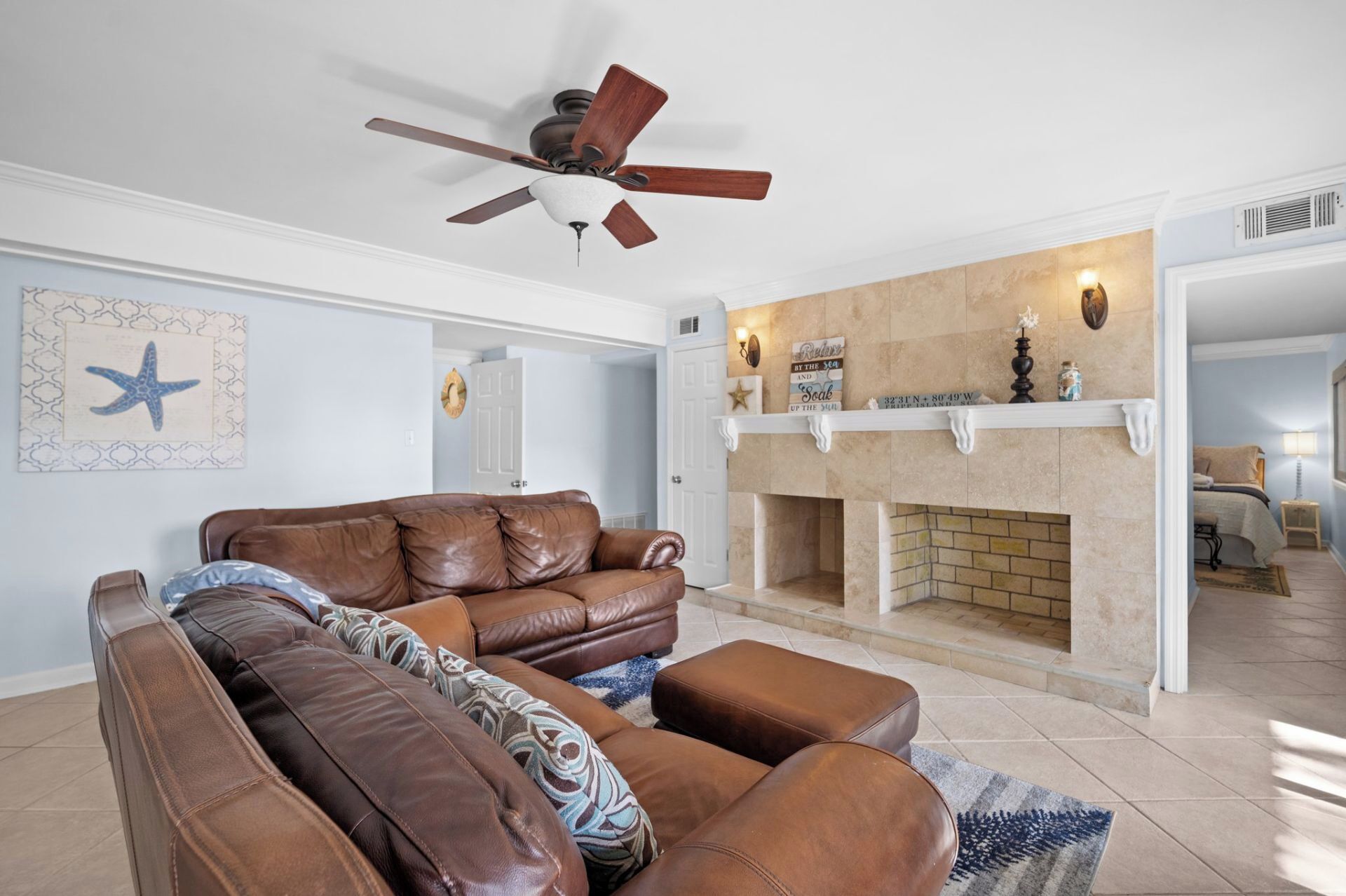 Ein Wohnzimmer mit braunem Ledersofa, Deckenventilator und Kamin.
