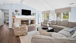 A spacious living room with a fireplace, a television, and a ceiling fan. - FrippLife, Walk to Beach, Golf Cart Included - 707 Bluefish (Fripp Island)