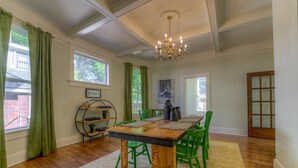 A dining area with a wooden table, green chairs, a chandelier, and a view of the outside. - Funky Memphis Game House! FirePit, Gtd pkg, Games! (Memphis)