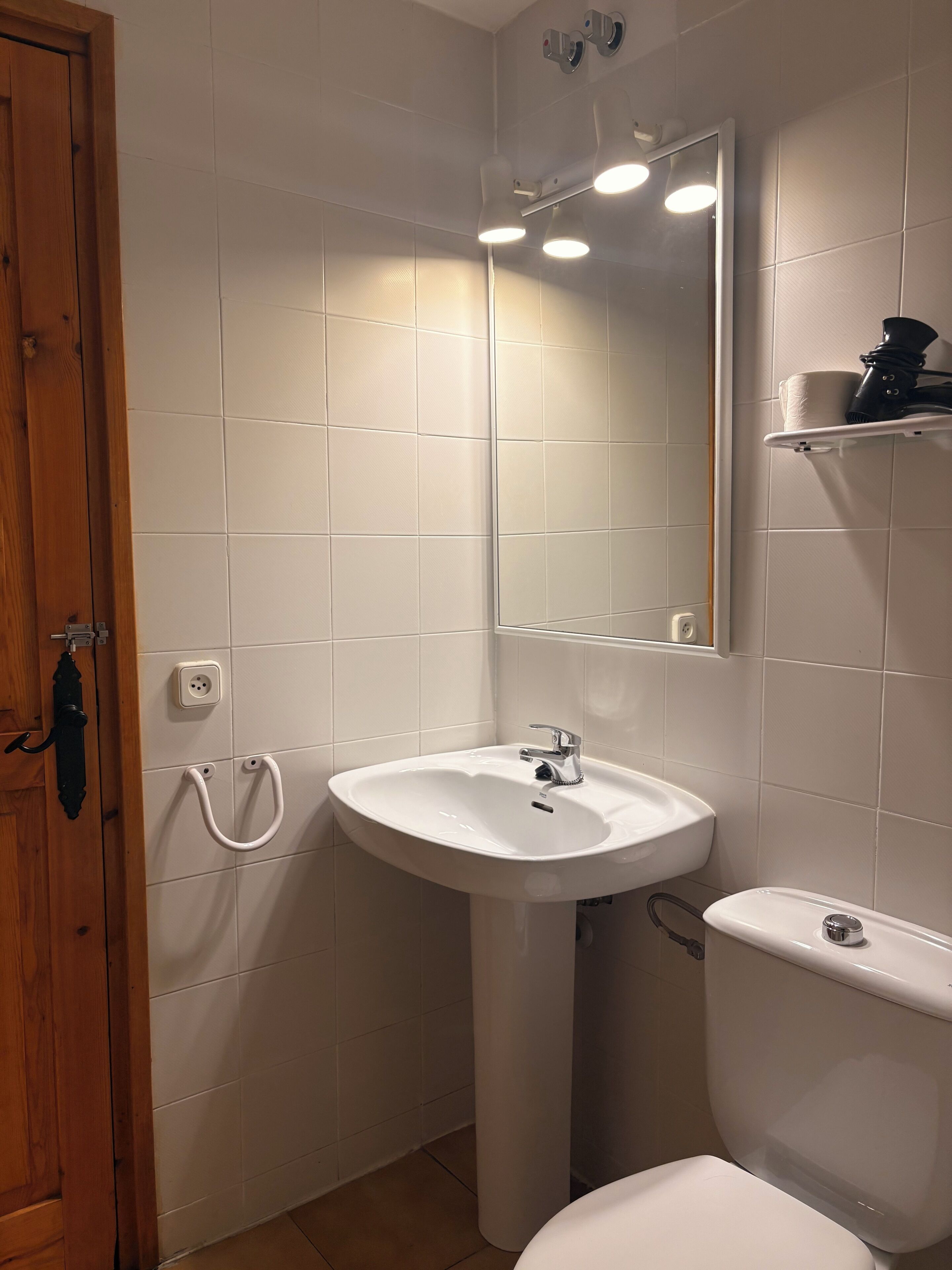 Ein Badezimmer mit Waschbecken, Spiegel, Toilette und Holztür.