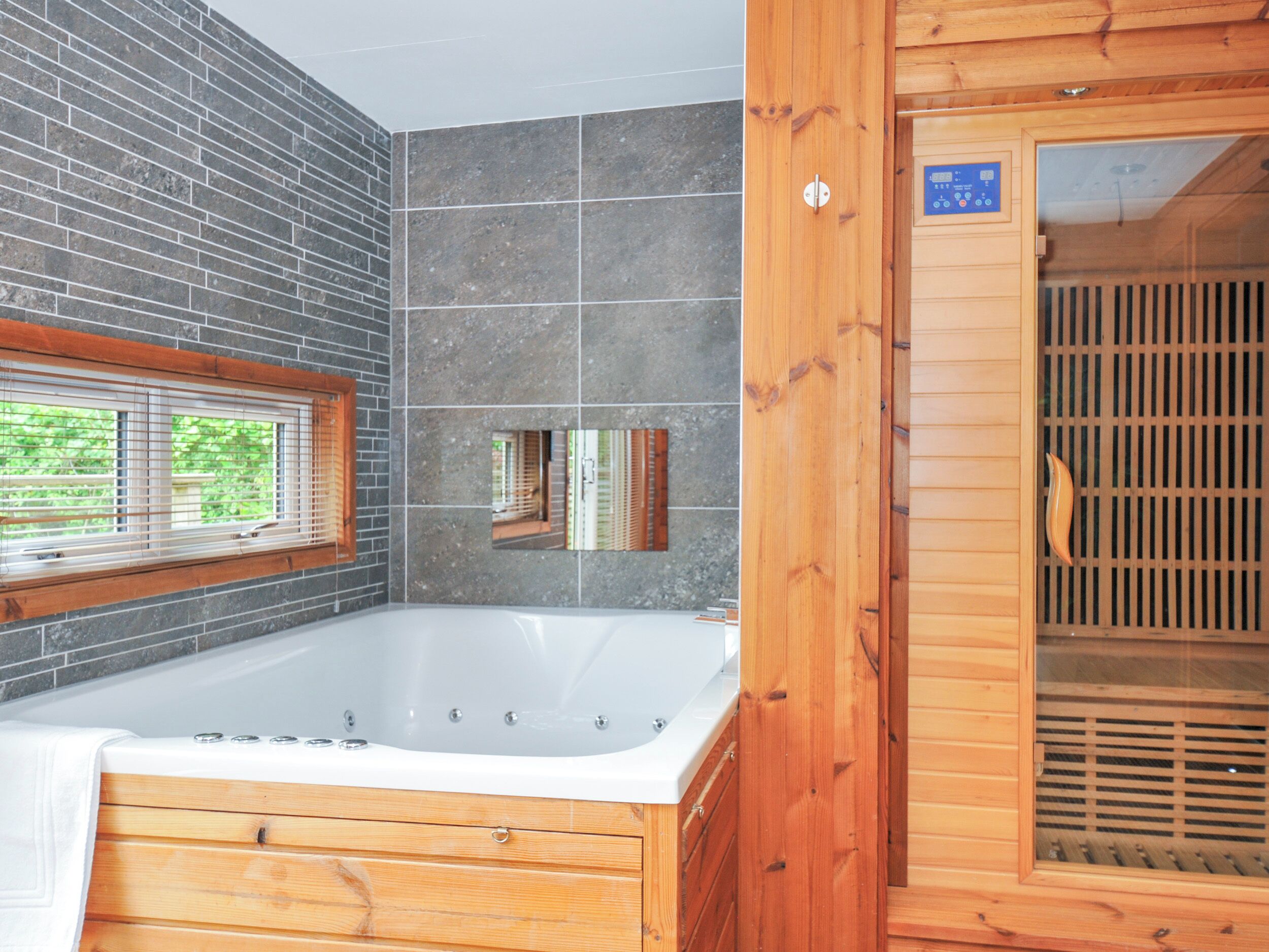 A modern bathroom with a large bathtub, wooden paneling, and a window with blinds.