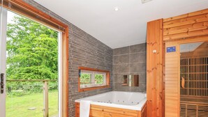 Un baño moderno con bañera de madera, mampara de ducha de vidrio y vistas a un jardín verde.