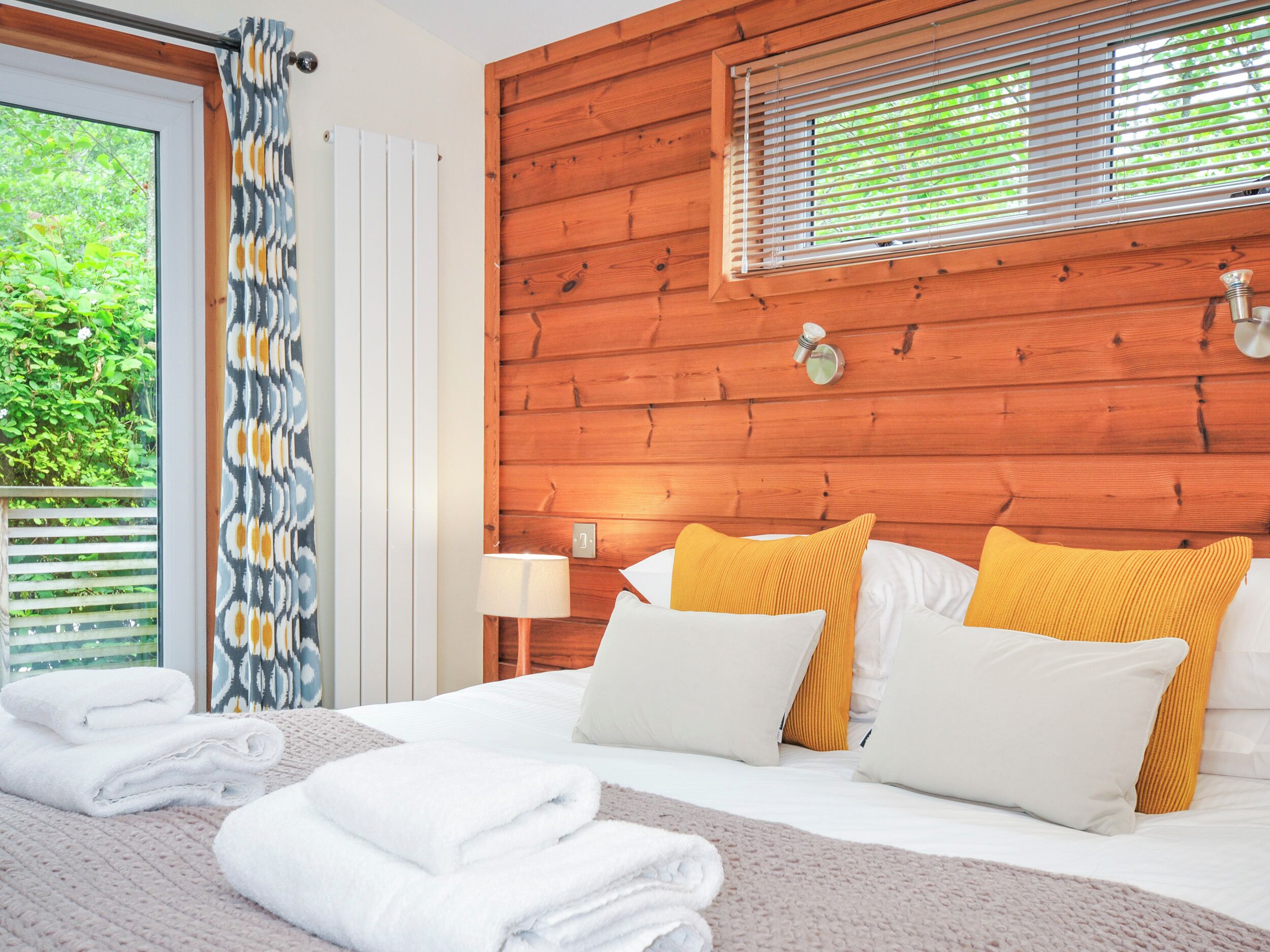 A neatly made bed with white and yellow pillows, a wooden headboard, and a window with blinds.