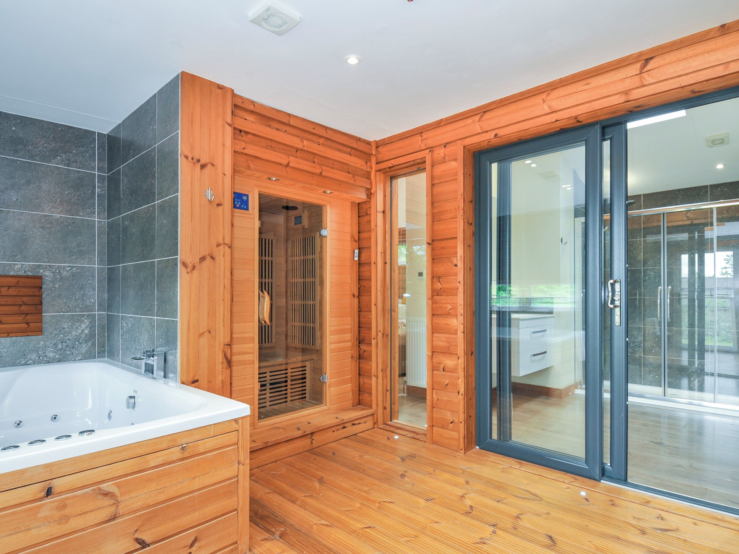 Un baño moderno con detalles de madera, una bañera grande y un box de ducha de vidrio.