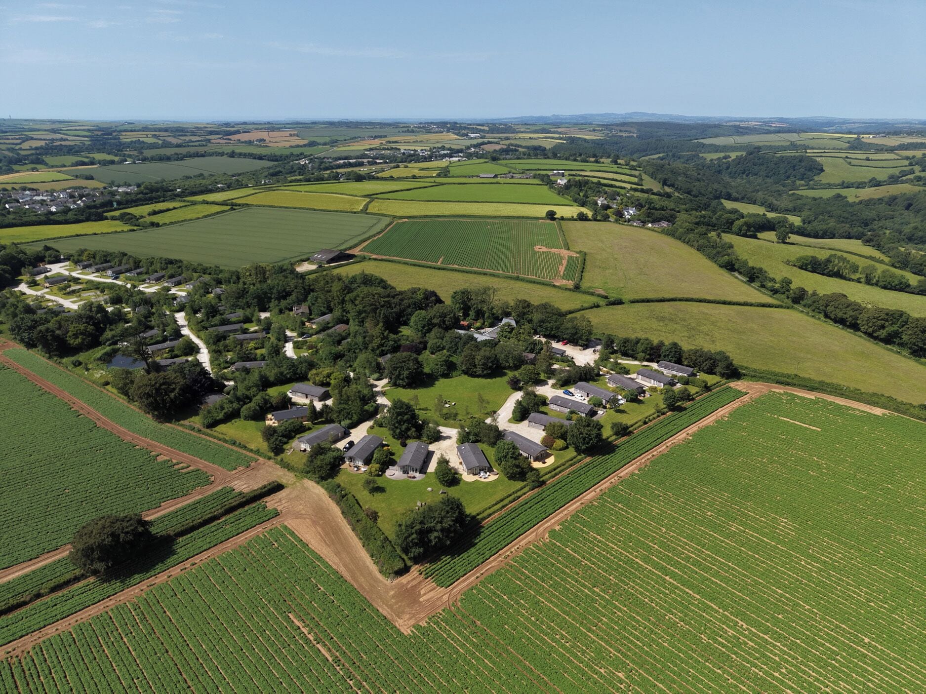 Vista aérea de una zona rural con campos, un grupo de casas y una masa de agua.