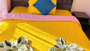 Una cama bien hecha con una colcha amarilla, un cabecero marrón y una almohada azul.