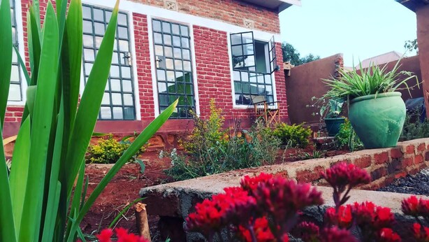 Un edificio de ladrillo con ventanas amplias, un jardín con flores rojas y plantas verdes.