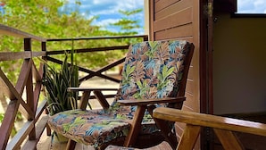 A wooden deck with two chairs featuring a tropical leaf pattern, a thatched roof, and a view of trees and sky. - Residencial Bem te vi (Jijoca de Jericoacoara)