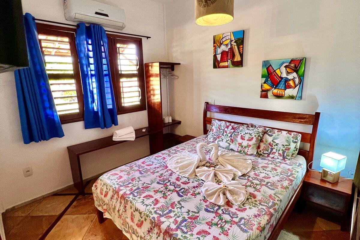 A neatly arranged bedroom with a bed, a bedside table, a nightstand, a wall-mounted TV, and a window with curtains.