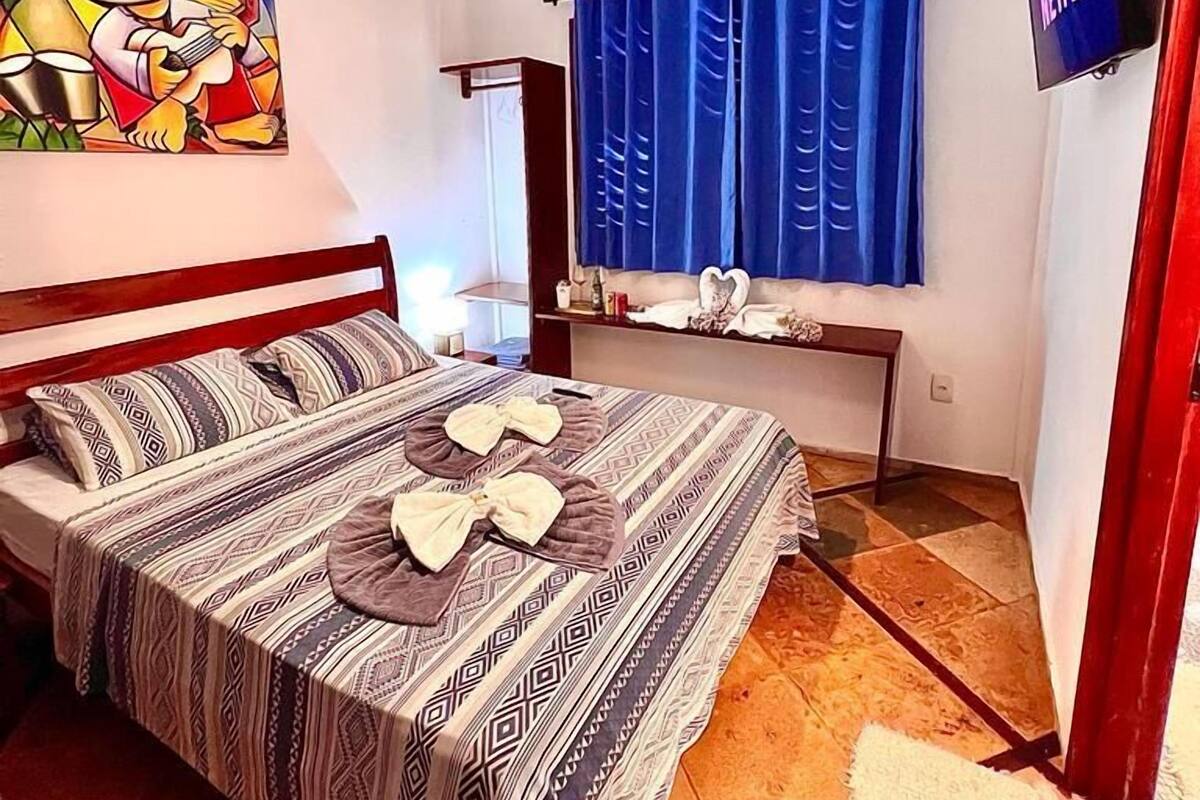 A bedroom with a bed, a TV, a painting, and a window with curtains.
