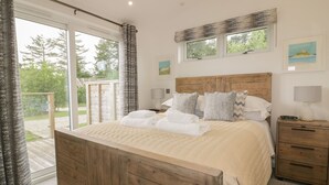 A bedroom with a wooden bed, a nightstand, and a view of the outdoors. - 7 Faraway Fields (Liskeard)