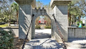 A stone archway with chains, leading to a pathway in a park.