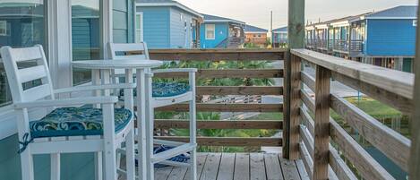 A wooden deck with a white chair and a table, overlooking a row of blue cabins.