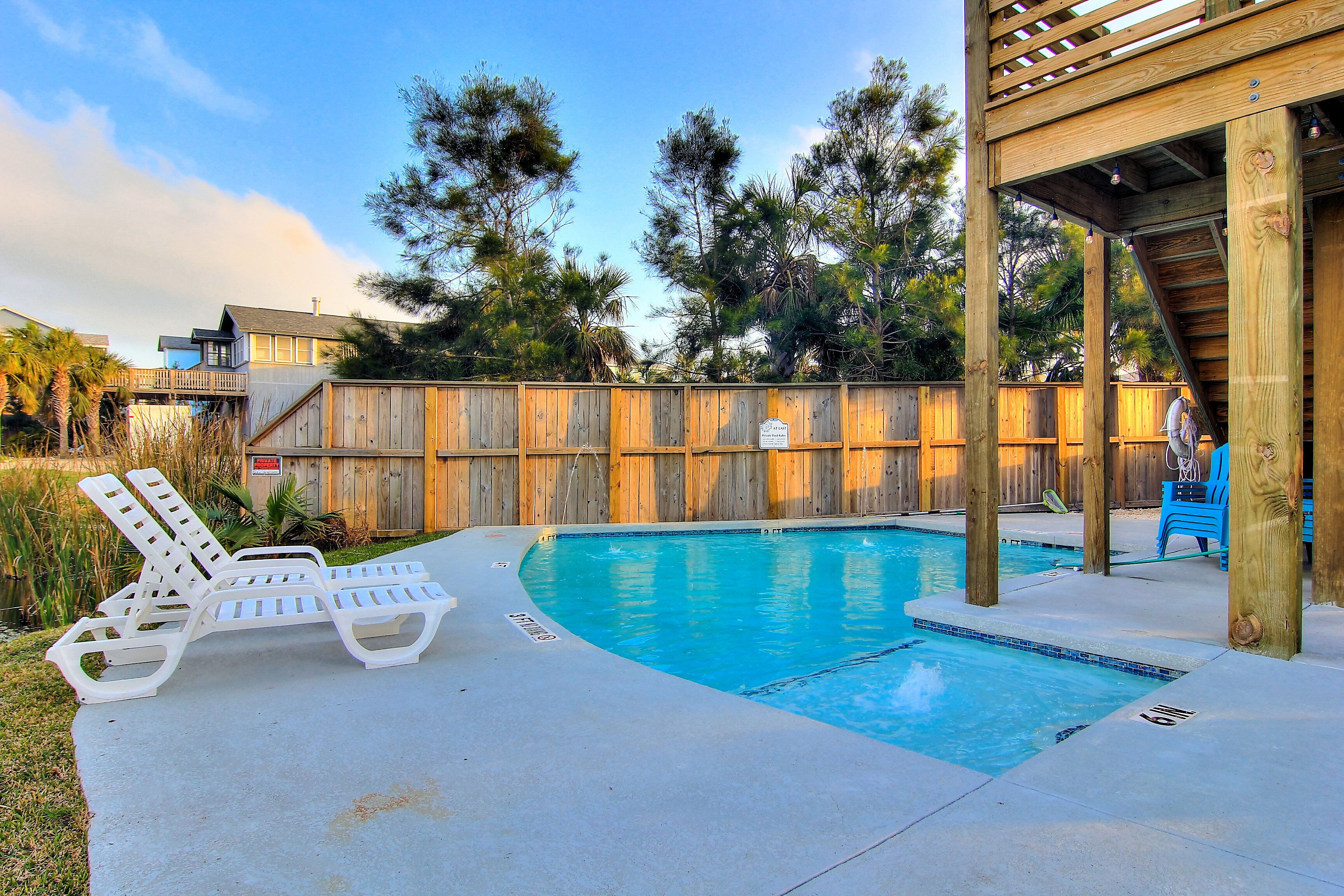 A swimming pool with lounge chairs, a wooden deck, and a wooden fence.