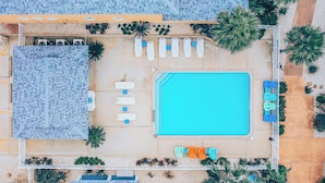 Vista aérea de um hotel com piscina, espreguiçadeiras e uma área coberta com cadeiras.