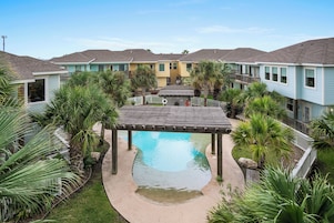 A residential complex with a central pool, surrounded by palm trees and a wooden deck.