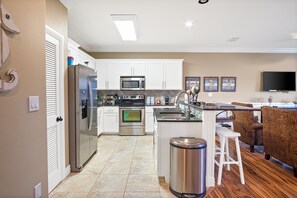 A modern kitchen with white cabinets, stainless steel appliances, a built-in oven, and a large island with stools.