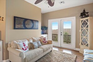 A living room with a beige sofa, decorative pillows, a round rug, and a view through a sliding glass door to an outdoor area.