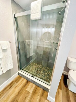 Bathroom features a glass-enclosed shower area with a showerhead mounted on the wall and a toilet with a visible pipe.