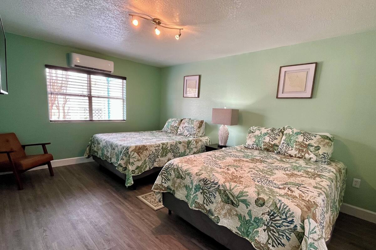 A room with two beds, a chair, and a window with blinds.