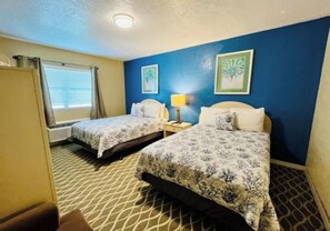 A hotel room with two beds, a window with blinds, a nightstand with a lamp, and two framed pictures on the wall. - Fiddler's Restaurant and Resort (Steinhatchee)