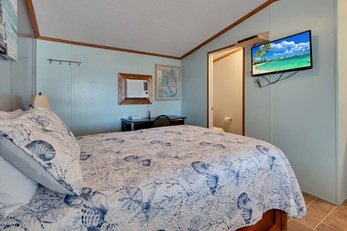 A bedroom with a bed, a desk, a chair, a mounted TV, and a wall-mounted air conditioner.