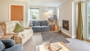 Una sala de estar con sofá, sillón gris, mesa de centro, chimenea y estantería.