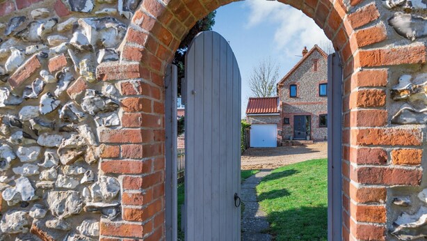 Un arco de piedra que da a una puerta blanca, con una casa de ladrillo y un garaje al fondo.