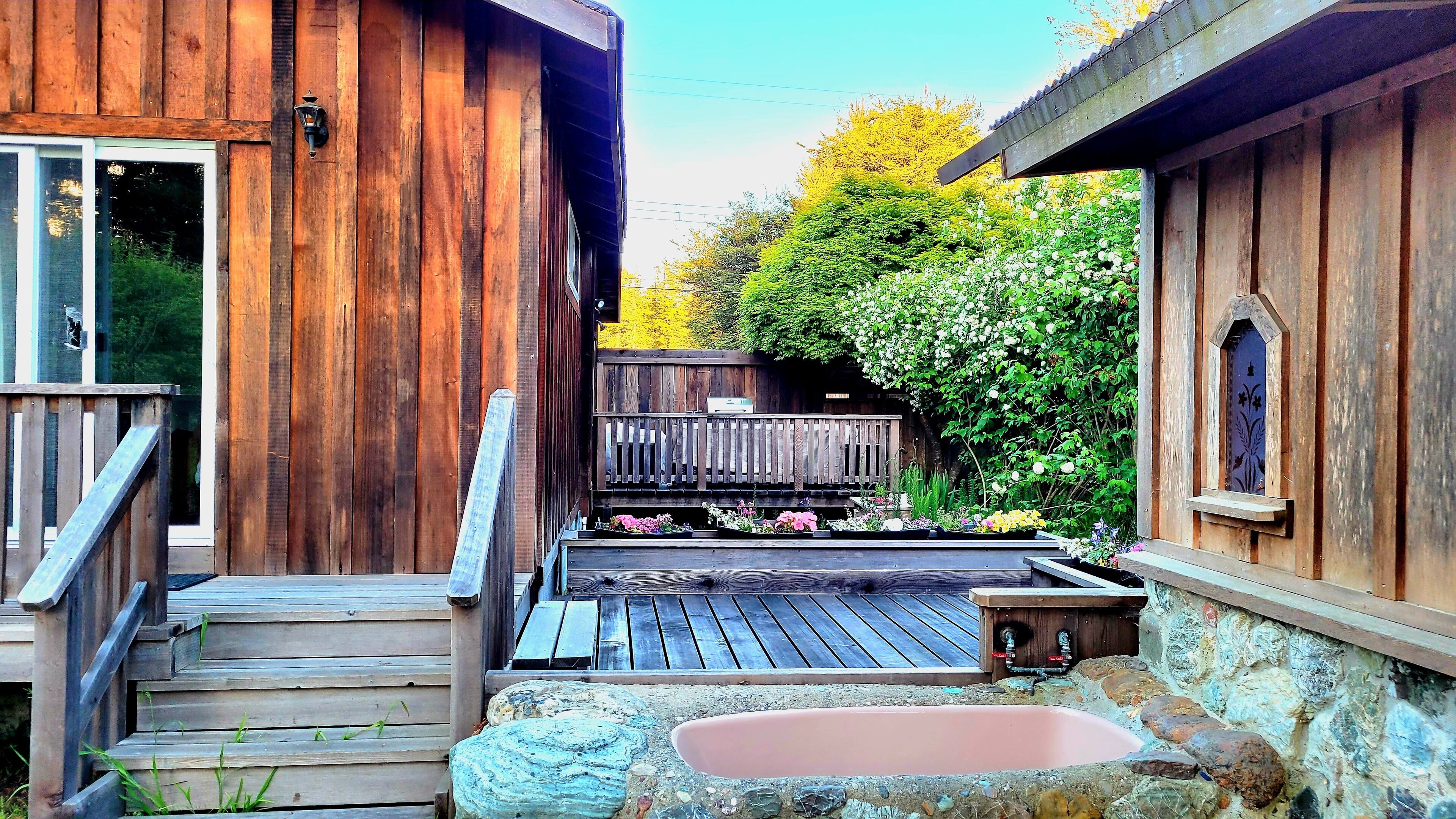 Une cabane en bois dotée d’une terrasse, d’un bain à remous et d’un jardin agrémenté de fleurs et d’arbustes.