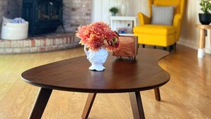 A round wooden table with a white vase of flowers in the center, a yellow armchair, and a wooden cabinet in a room with wooden beams and a brick wall. - Mendocino Coast Home with Sauna and Fireplace  (Fort Bragg)