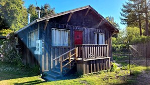 A rustic wooden cabin with a red door, a small porch, and a staircase leading to the entrance. - Mendocino Coast Home with Sauna and Fireplace  (Fort Bragg)