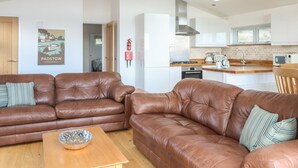 A modern living room with two brown leather sofas, a wooden coffee table, and a kitchen in the background. - 14 Faraway Fields (Liskeard)
