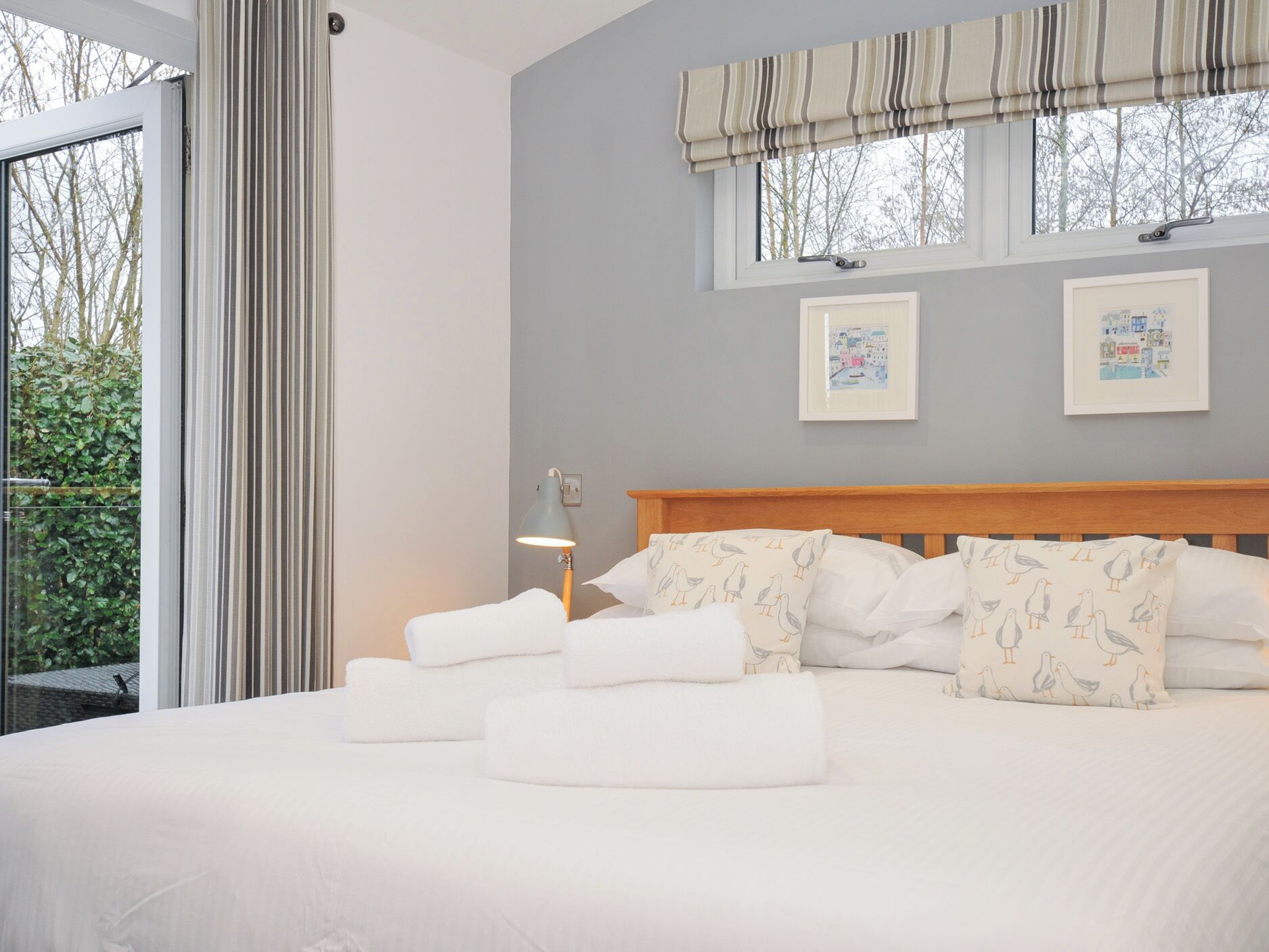 A neatly made bed with white linens and pillows, a wooden headboard, and two framed pictures on the wall.