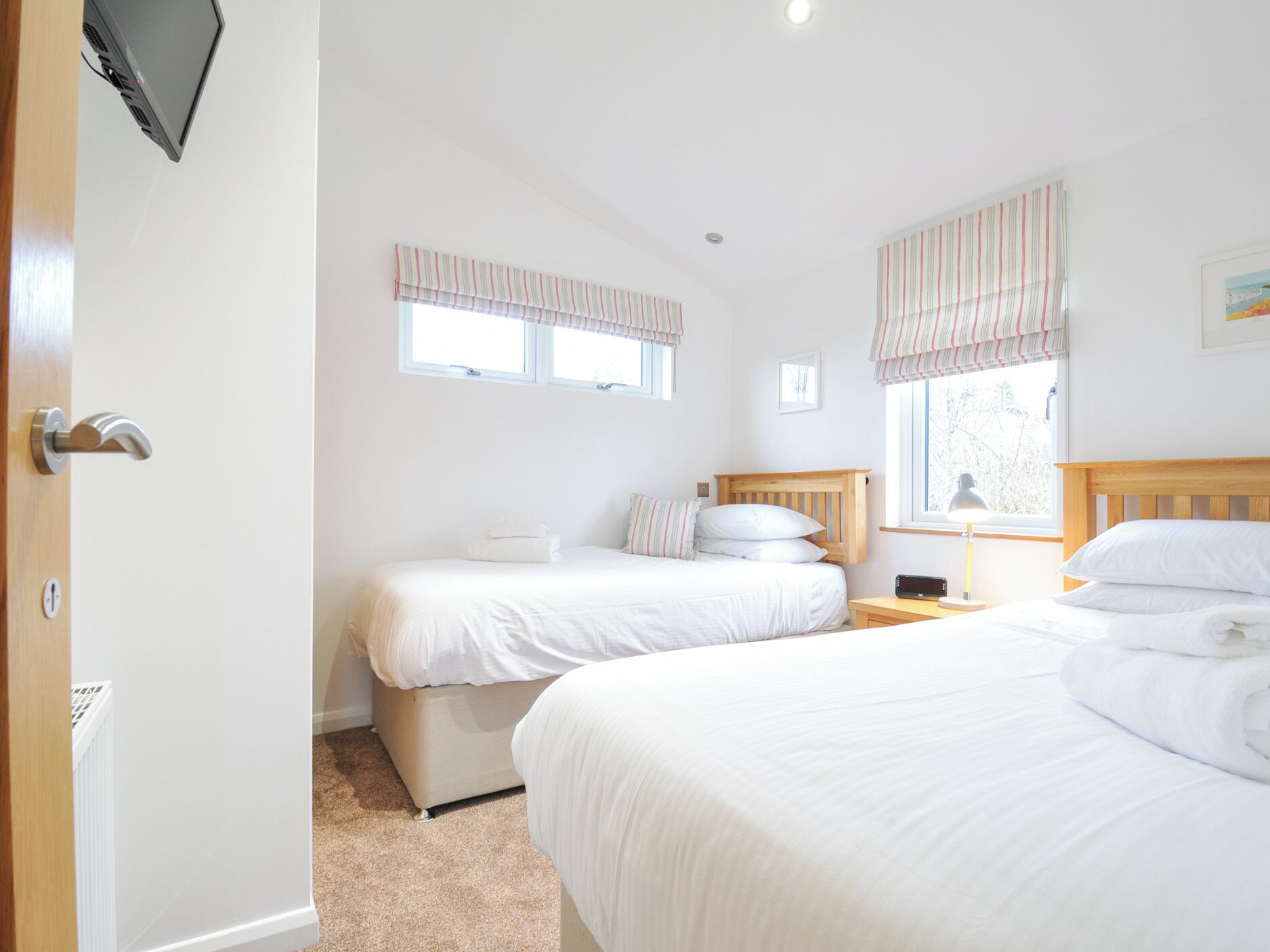 A bedroom with two beds, a wooden headboard, a bedside table with a lamp, and a window with striped curtains.