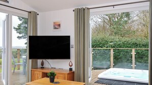 Ein modernes Wohnzimmer mit Flachbildfernseher, Holzmöbeln und einer Schiebeglastür, die zu einem Whirlpool und einem Außenbereich führt.