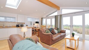 Ein geräumiges Wohnzimmer mit braunem Ledersofa, einem Holztisch und einem Essbereich mit Tisch und Stühlen. Ein großes Fenster bietet Blick ins Freie.