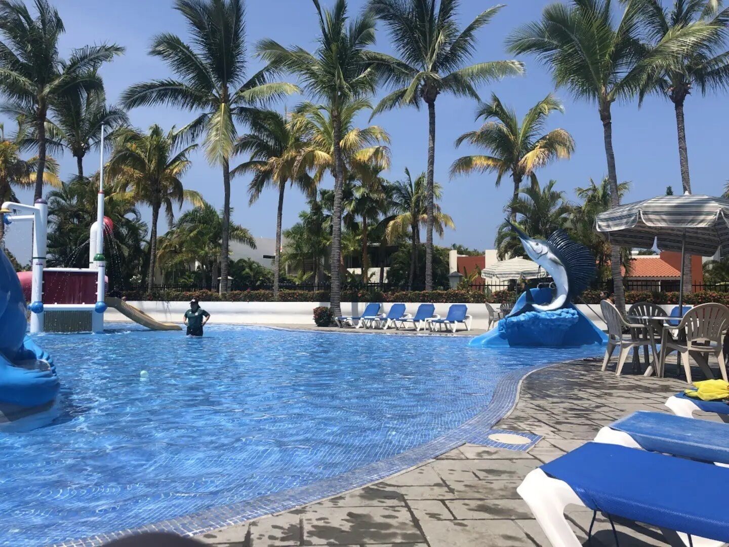 A swimming pool with water slides, lounge chairs, and palm trees.