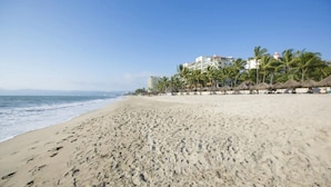 A wide sandy beach with footprints, palm trees, and a building with multiple floors in the background. - CONDO MARINA G  BY TRVL2HM (Nuevo Nayarit)