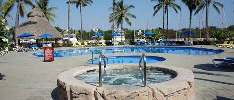 Zona de piscina con jacuzzi, sillas de descanso y palmeras.