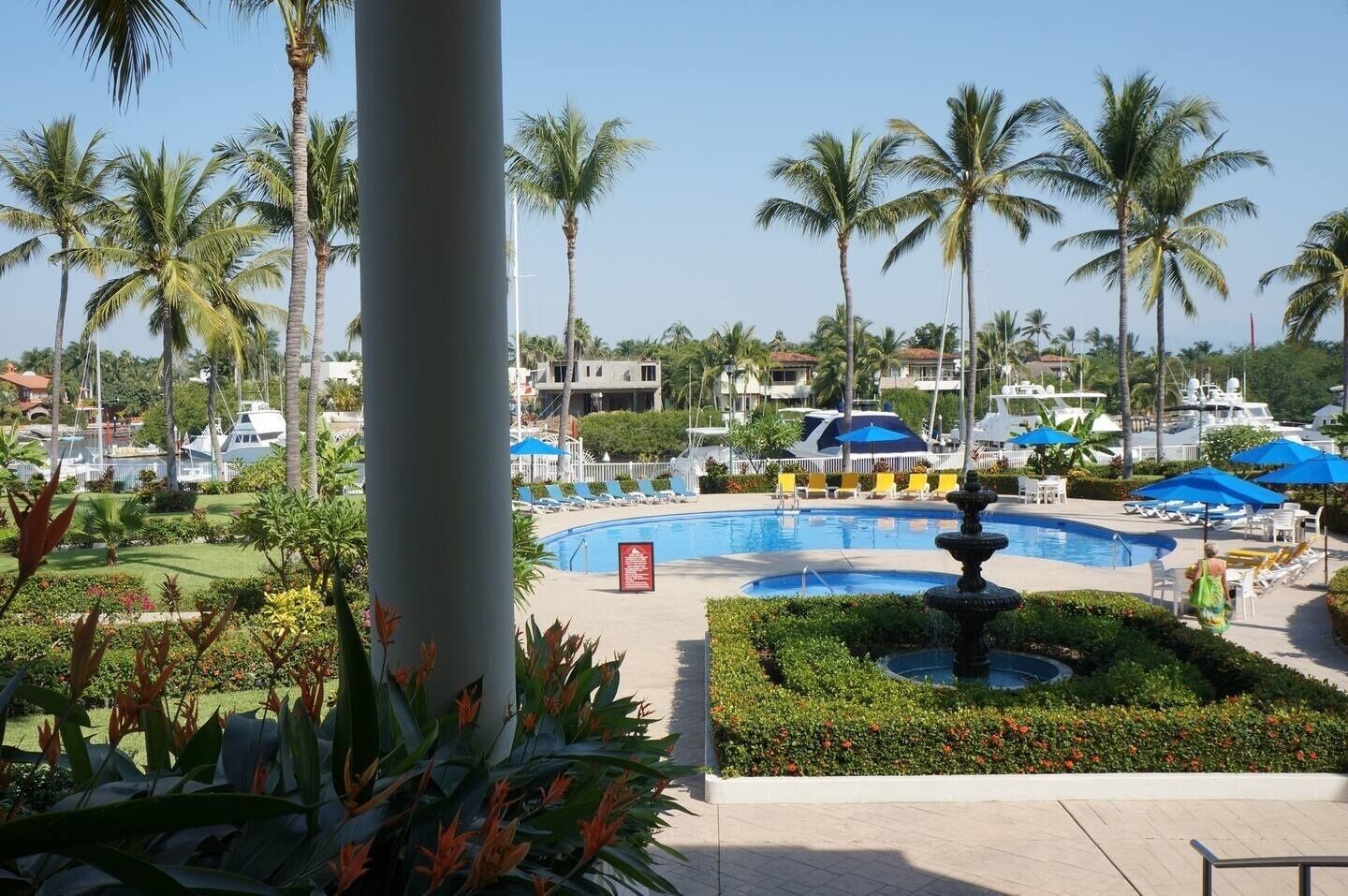 Un área de piscina con palmeras, sillas de descanso y una fuente.