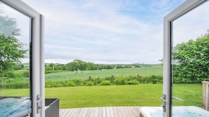 Une terrasse en bois avec un jacuzzi et une porte vitrée donnant sur un paysage verdoyant et luxuriant.