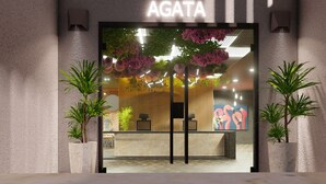 L’entrée d’un hôtel, avec un comptoir d’accueil, deux plantes en pot et une enseigne sur laquelle on peut lire « AGATA ».