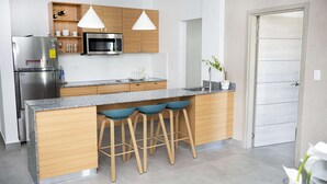 Une cuisine moderne équipée d’un réfrigérateur en acier inoxydable, d’un four à micro-ondes, de meubles en bois, d’un plan de travail en granit et de trois tabourets de bar bleus.