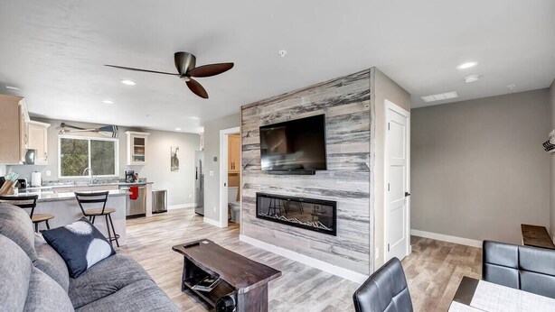 A modern living room with a fireplace, a large TV mounted on a stone wall, and a dining area with a table and chairs.