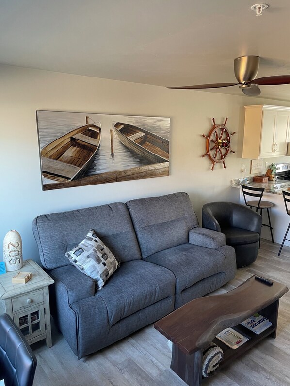 A living room with a gray sofa, a wooden coffee table, a ship's wheel decoration, and a ceiling fan. - CONDO 7-Coastal Chic Condo in the Heart of Sister Bay! (Sister Bay)