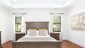 A bedroom with a large bed, two bedside tables, a window with curtains, and a painting on the wall.