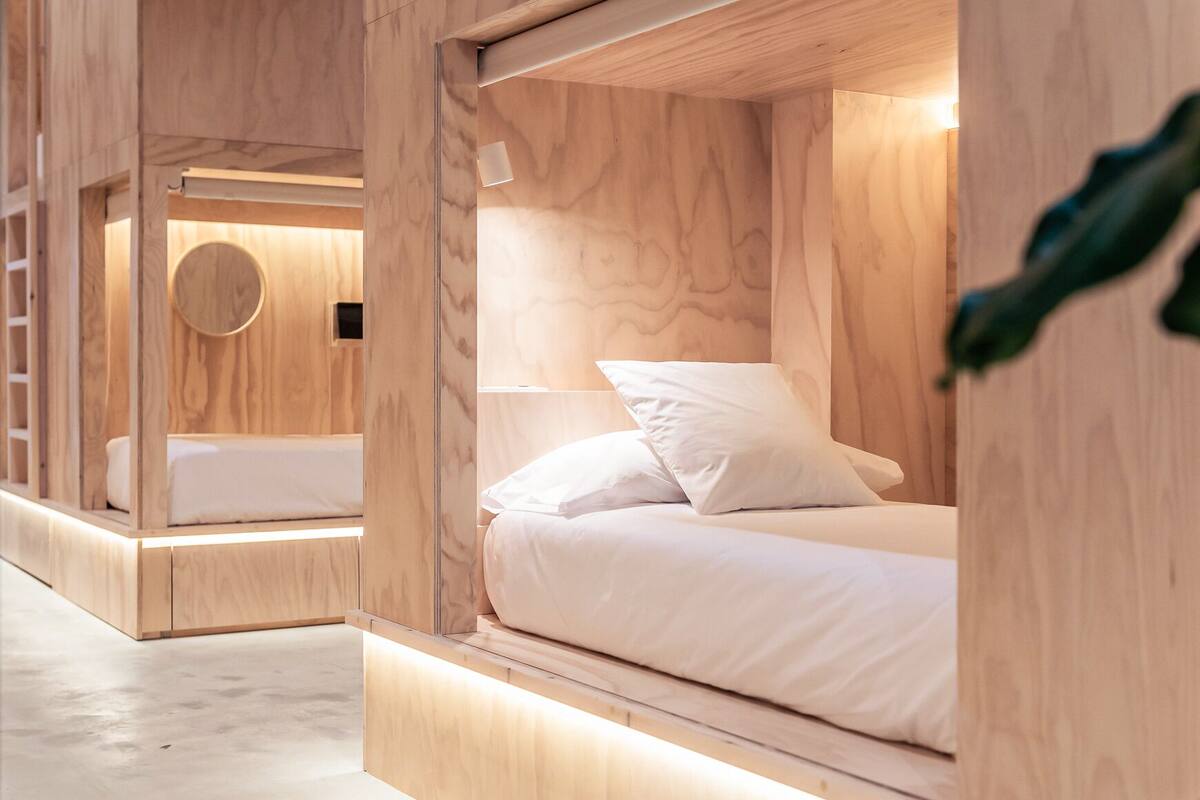 A modern, minimalist room with two bunk beds made of wood, a circular window, and a small round table.