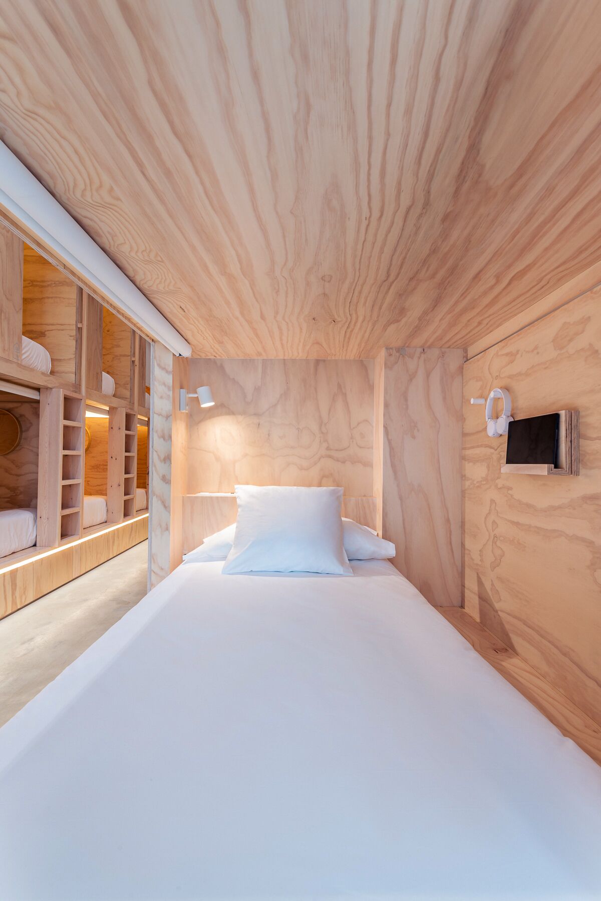 A modern bedroom with a wooden ceiling, a large bed with white linens, a built-in wardrobe, and a bedside table with a lamp.